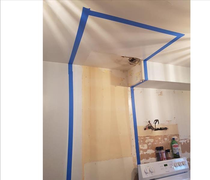 ceiling and wall in a kitchen showing blue tape for treament area and a hole from mould damage in the ceiling