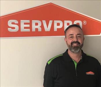 Angelo in a black jacket SERVPRO, grey trimmed beard in front of the logo