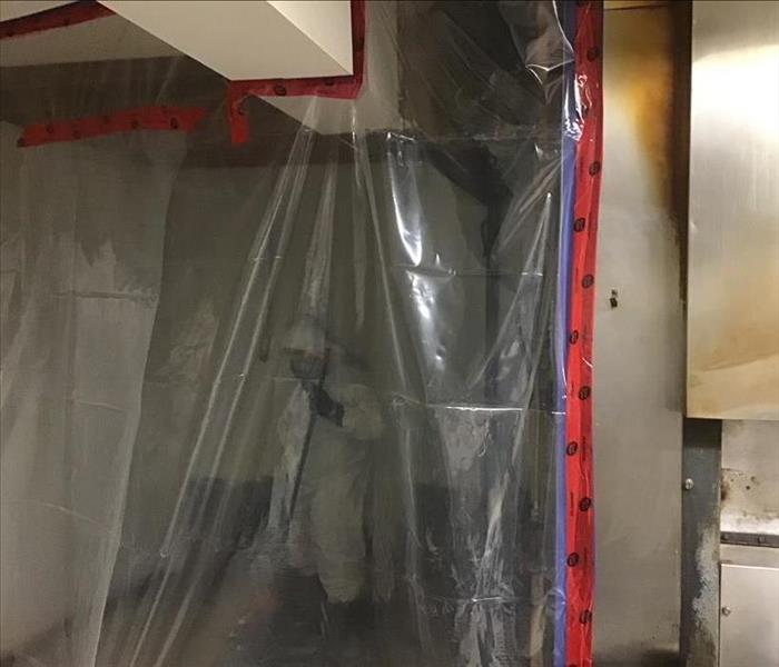 Tech in Tyvek suit behind containment barrier cleaning